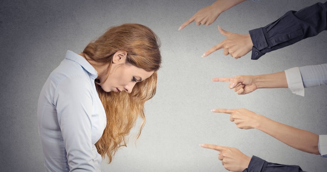 Mulher triste com várias mãos sendo apontadas para ela.